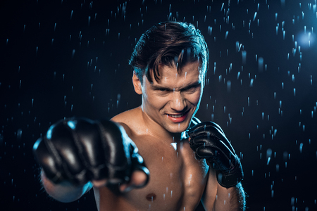 Selective focus on boxer in leather gloves standing under water drops on black backgroundの写真素材
