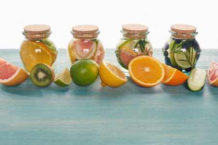 Detox drinks in jars with fruits, vegetables, herbs, berries and greenery near ingredients on wooden blue surface isolated on white backgroundの写真素材