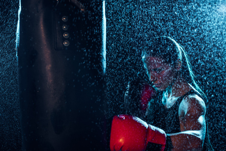 Strong boxer in red boxing gloves training under water drops on black backgroundの写真素材