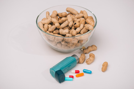 Glass bowl with tasty peanuts near blue inhaler and pills on grey backgroundの写真素材
