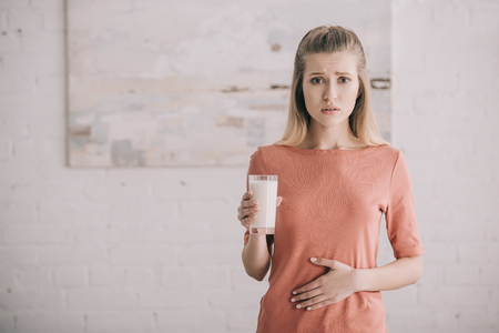 Upset woman with lactose intolerance holding glass of milkの写真素材