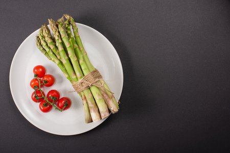 Top view of green asparagus and cherry tomatoes on plate on black backgroundの写真素材