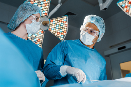 Nurse in uniform and surgeon in medical cap looking at each other in operating roomの写真素材