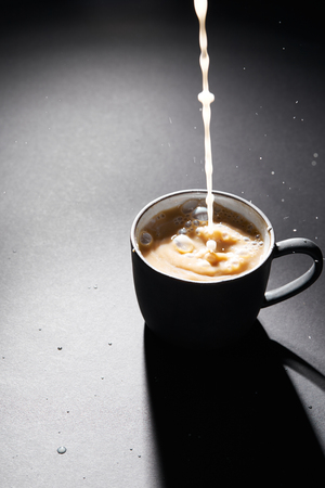 Cup of coffee with pouring milk on dark textured surfaceの写真素材