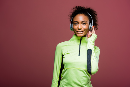 Beautiful African american sportswoman in headphones looking at camera isolated on brown with copy spaceの写真素材