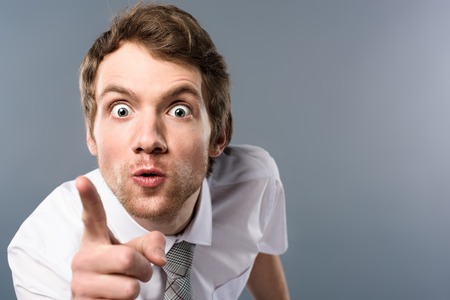 Aggressive businessman with funny face expression pointing with finger at cameraの写真素材