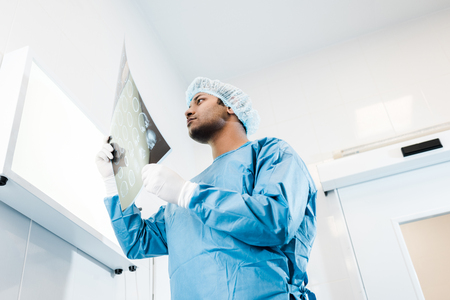 Low angle view of doctor in medical cap and latex gloves looking at x-rayの写真素材