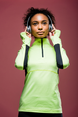 Beautiful African American sportswoman in headphones and track jacket isolated on brown backgroundの写真素材