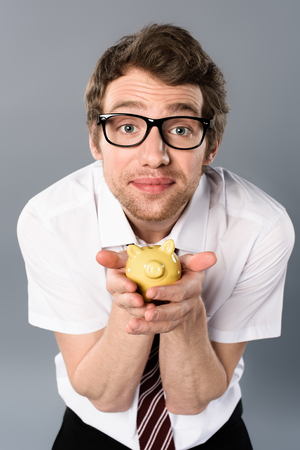 Handsome businessman in glasses holding piggy bank on grey backgroundの写真素材