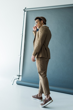 Fashionable mixed race man in suit and hat posing on grey backgroundの写真素材