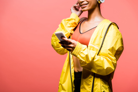 Cropped view of African American sportswoman using smartphone isolated on coral with copy spaceの写真素材
