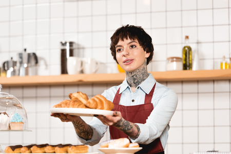 Smiling barista holding dish with croissants in outstretched handsの写真素材