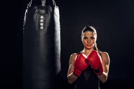 Front view of boxer in red boxing gloves standing near punching bag on black backgroundの写真素材