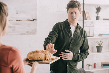 Cropped view of woman holding cutting board with sliced bread near handsome man with gluten allergyの写真素材