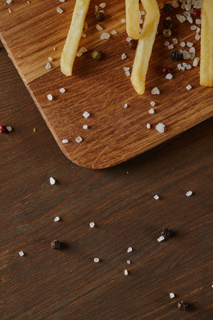 Top view of salt, black pepper and fresh golden french fries on wooden chopping boardの写真素材