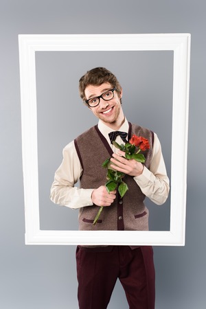 Smiling man in white frame holding bouquet of roses on grey backgroundの写真素材
