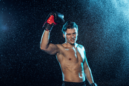 Smiling boxer standing with hand up under water drops on black backgroundの写真素材