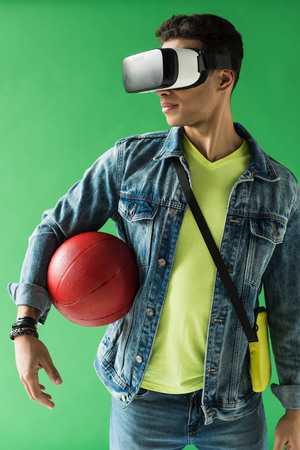 Mixed race man in virtual reality headset holding basketball on green screenの写真素材
