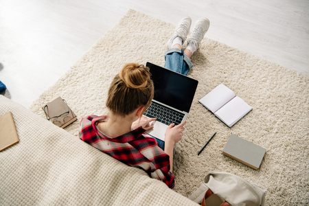 Overhead view of teenager with books and laptop with blank screen doing homeworkの写真素材