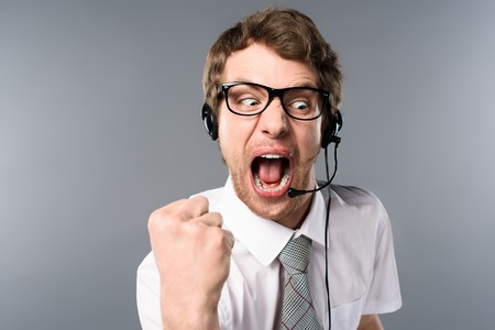 Angry call center operator in headset and glasses yelling and showing fist on grey backgroundの写真素材