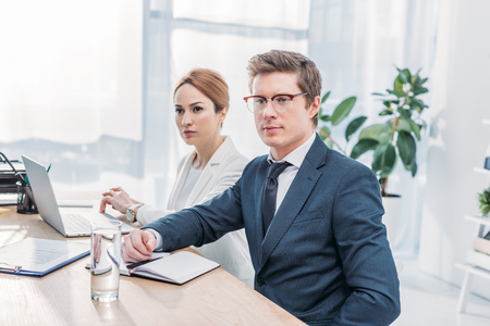 Handsome recruiter in glasses sitting with attractive coworker in officeの写真素材