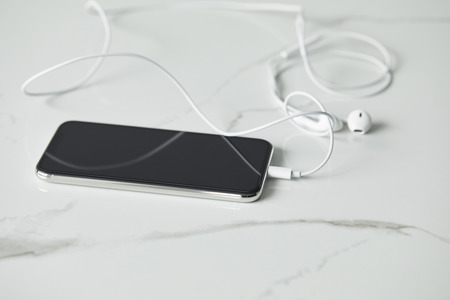 Selective focus of smartphone with connected earphones on white marble surfaceの写真素材