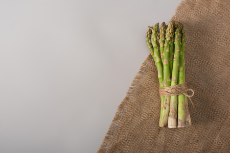 top view of bunch of green asparagus tied with rope near sackcloth on grey backgroundの写真素材