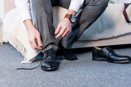 partial view of man putting on black leather shoes while sitting on beddingの写真素材