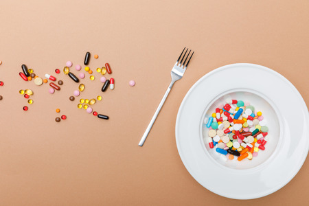 Top view of bowl with pills and fork on brown surfaceの写真素材