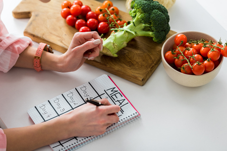 cropped view of girl writing in notebook with meal lettering near ingredients in kitchenの写真素材