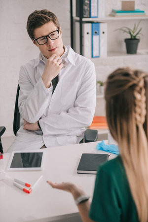 Back view of blonde patient sitting near pensive doctor in glasses and white coatの写真素材