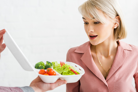 Cropped view of man holding takeaway box with vegetables near surprised young womanの写真素材