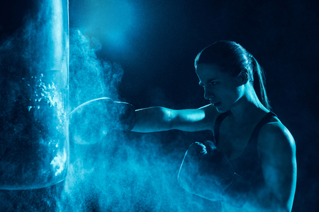 Female boxer in boxing gloves training with punching bagの写真素材