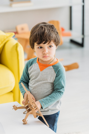 adorable serious child holding wooden plane model at homeの写真素材