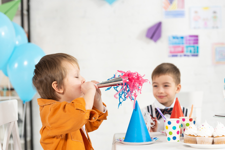 adorable preteen boys sitting at festive table with party horn and cupcakes during birthday celebrationの写真素材