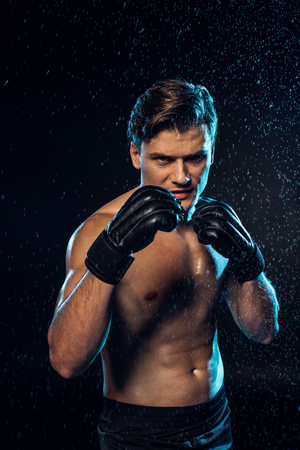 Front view of boxer in leather gloves standing under water drops on blackの写真素材