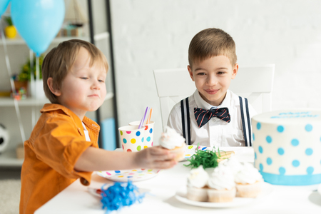 adorable preteen boys sitting at table with cupcakes during birthday partyの写真素材