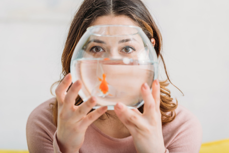 selective focus of woman holding aquarium with bright gold fish and looking at cameraの写真素材