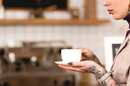 partial view of tattooed businesswoman holding coffee cup in cafeの写真素材