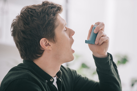 side view of handsome man using inhaler at homeの写真素材