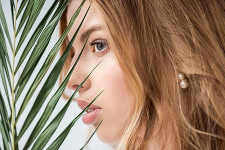 dreamy and attractive girl near green palm leaf on whiteの写真素材