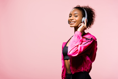 Beautiful smiling African American sportswoman in headphones looking at camera isolated on pink with copy spaceの写真素材