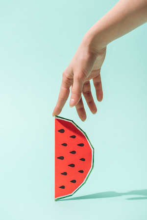 cropped view of young woman touching paper watermelon with seeds on turquoiseの写真素材