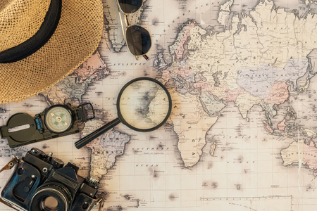 Top view of straw hat, film camera, compass, magnifier and sunglasses on world mapの写真素材