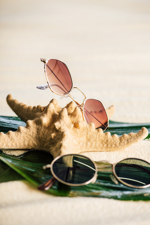 selective focus of sunglasses, green leaves and starfish on beachの写真素材
