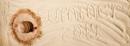 panoramic shot of summer 2019 written on wavy sand with straw hatの写真素材