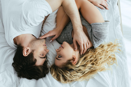 top view of blonde young woman touching face of boyfriend while  lying on bedの写真素材