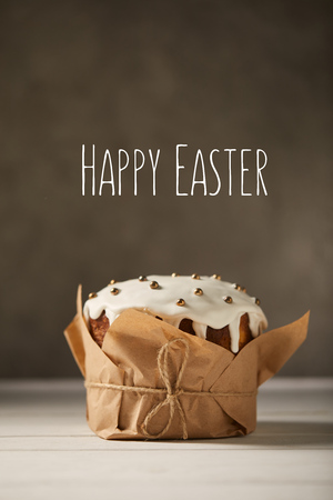 traditional decorated Easter cake in craft paper on white table with happy easter lettering on brown backgroundの写真素材