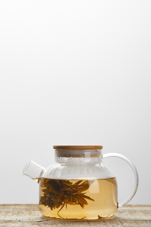 glass teapot with chinese blooming tea on wooden table isolated on grey with copy spaceの写真素材