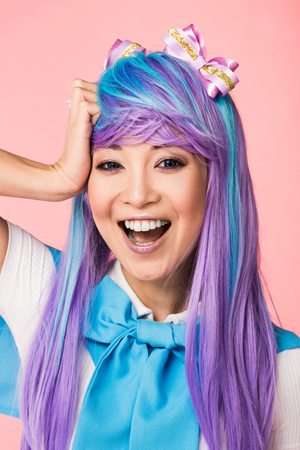 Laughing Asian anime girl in purple wig looking at camera on pink backgroundの写真素材